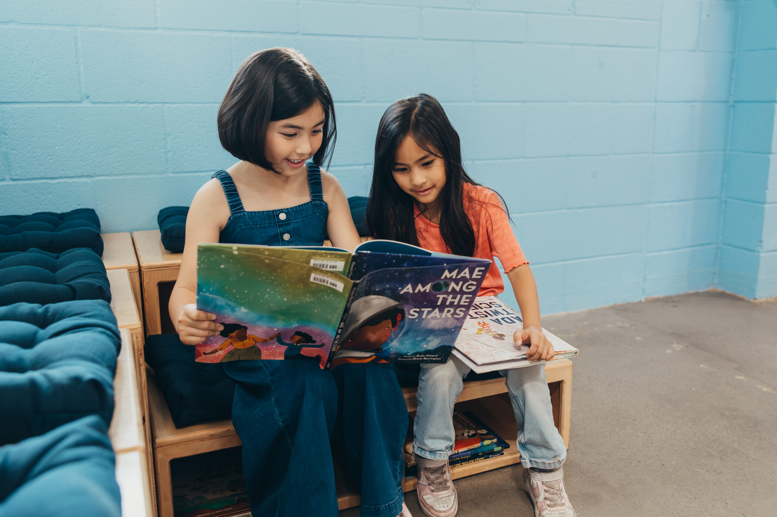 2 little girls sitting on bench reading a book together