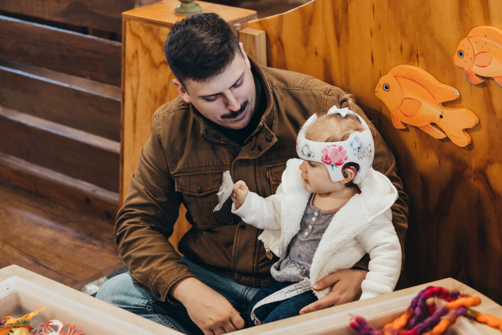 A child with a helmet plays with her father during Sensory Friendly Mornings.