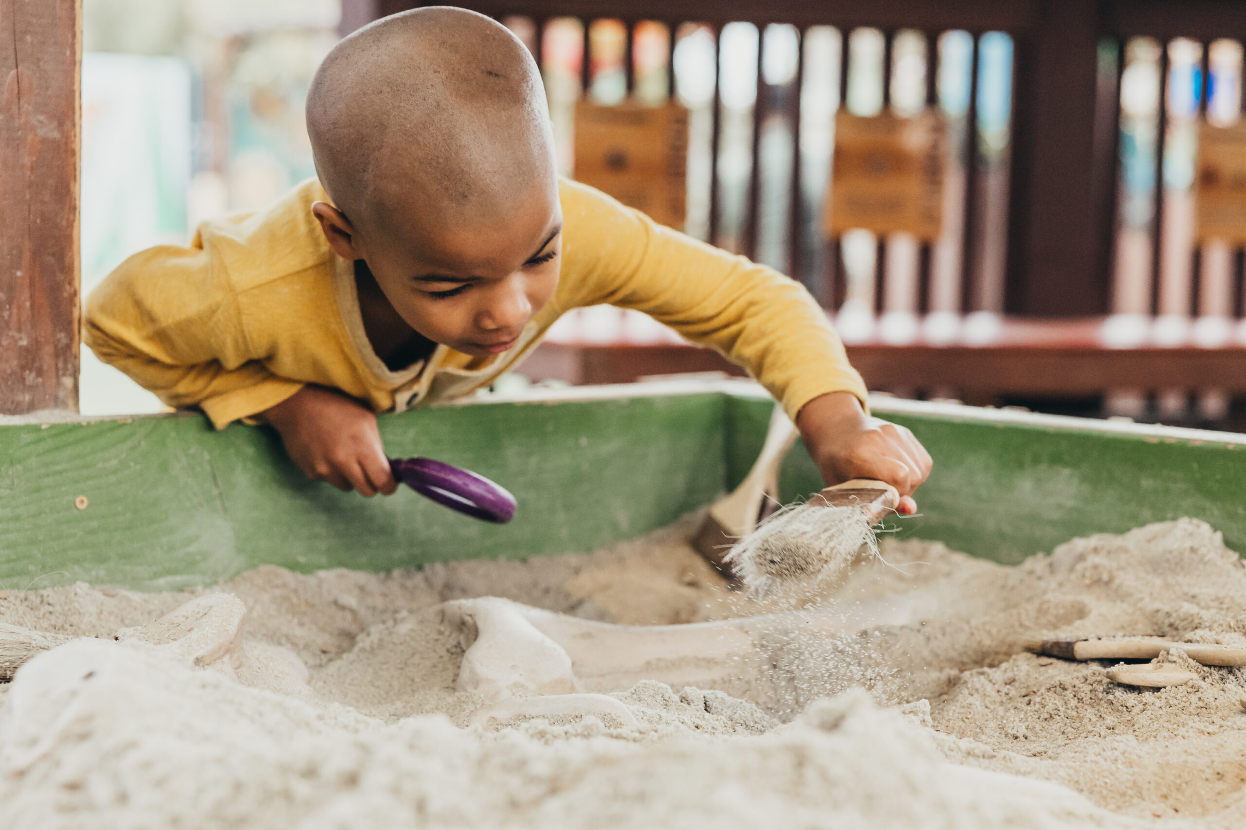 little boy playing in sand box with magnifying glass and paint brush