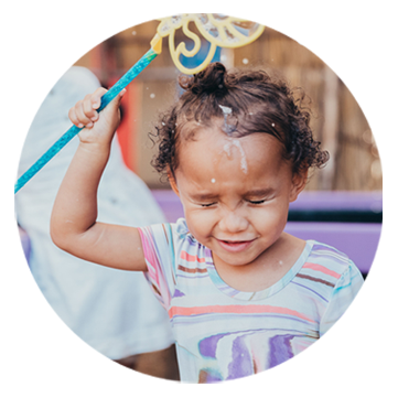 small girl pouring soap from bubble maker over her head with her eyes closed