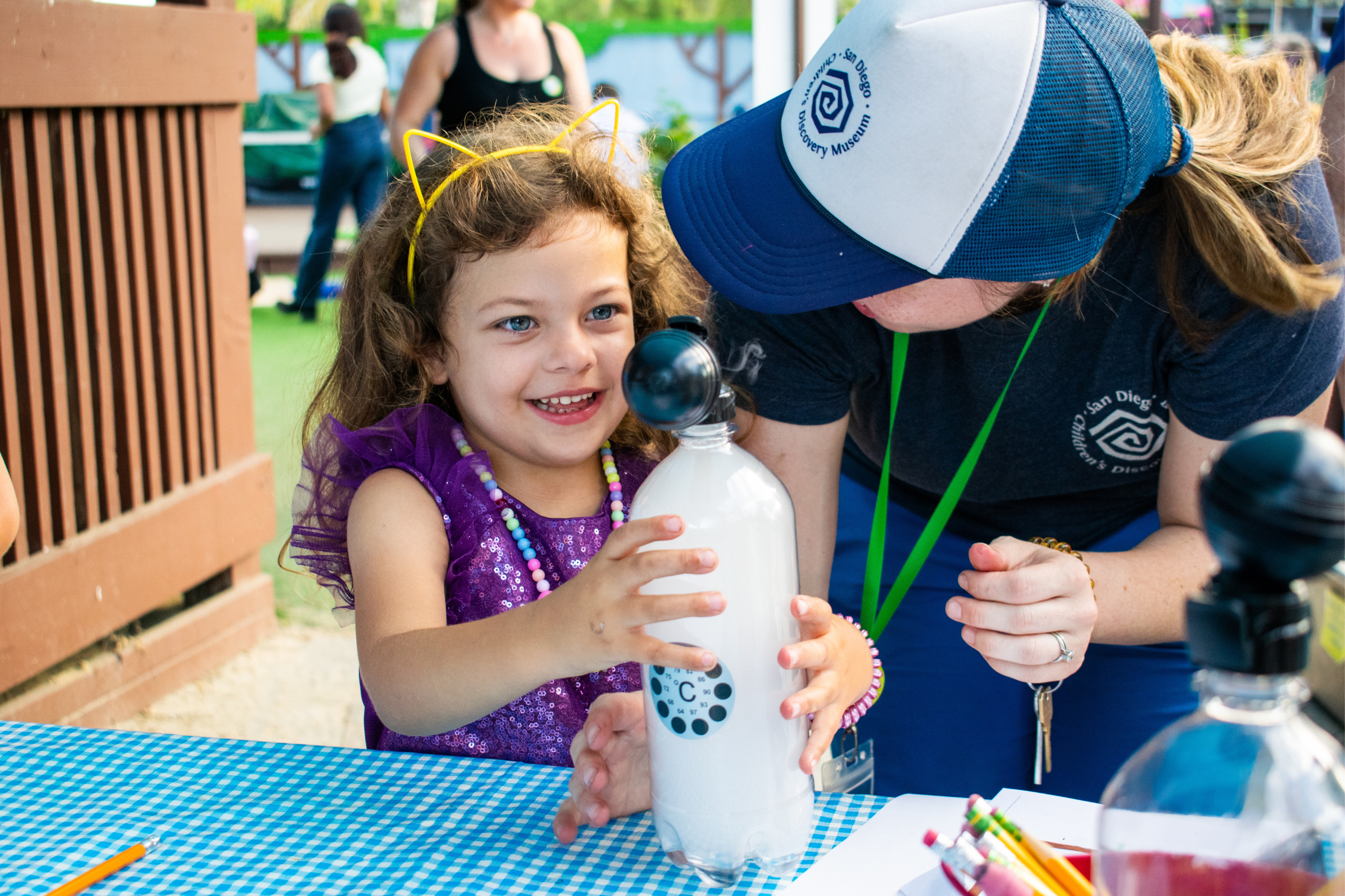 Little girl conducting a cloud in a bottle science experiment with an SDCDM staff member standing next to her.