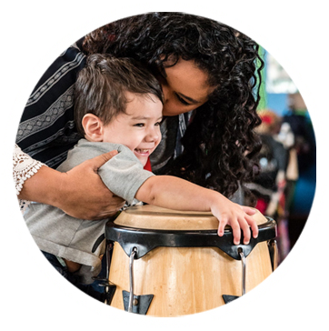 boy holding a bongo with mom hugging him