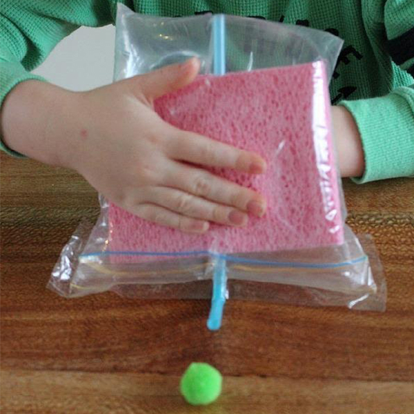 Child holding a plastic bag with a straw and sponge to create air pressure in a bag.