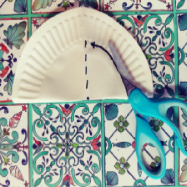 A paper plate folded in half and scissors cutting a half circle shape.