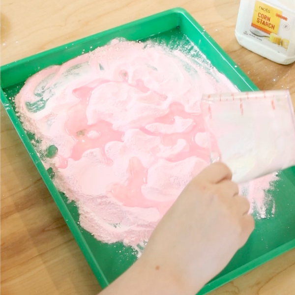 Oil being poured over combined craft sand and cornstarch.