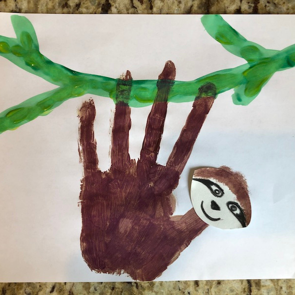 A brown painted handprint sloth on a green branch.